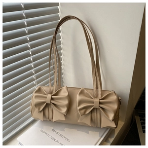 Detail view of a beige cylinder Boston bag with elegant bow decor on a book