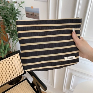 Macro shot of striped toiletry bag with zipper and woven fabric detail held by hand