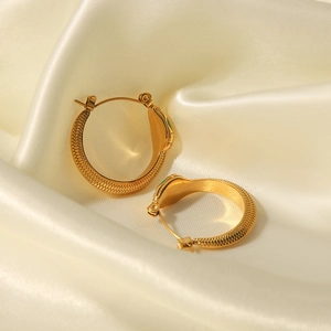 Elegant gold snake earrings with green gem eyes and scale texture on silk background