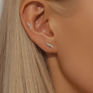 Close-up of S-shaped silver stud earrings with sparkling diamonds on female ear