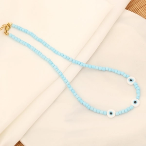 Handmade necklace with light blue beads, evil eye charms and gold clasp on white fabric
