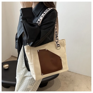 Detail of canvas tote bag with brown leather pocket and letter print shoulder strap