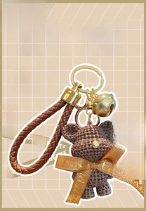 Detail of a brown resin bear keychain with a woven texture, gold bell, and leather strap