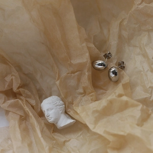 Detailed view of silver liquid teardrop stud earrings on textured vintage paper