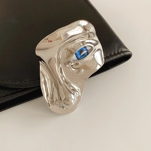 Macro detail of silver abstract face brooch with blue eye and rhinestone accents
