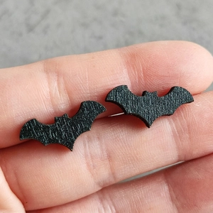 Close-up of textured black bat stud earrings for Halloween held by fingers for detail