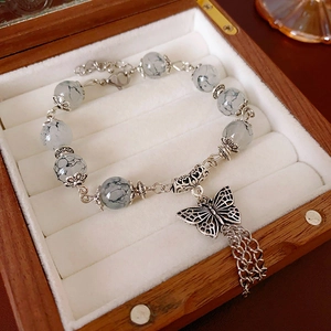 Détail du bracelet vintage en perles avec pendentif papillon évidé et pompons en métal