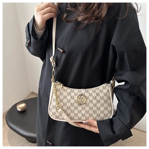 Detail view of cream-colored shoulder bag with monogram texture and golden M logo on model