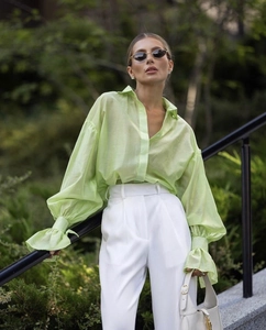 Detail of light green sheer chiffon blouse with flared cuffs and white high-waist trousers