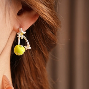 Close-up of a silver star earring with yellow zircon and apple-shaped drop on model