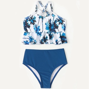 Two-piece girls bikini set with tropical palm tree print and ruffled hem on blue background