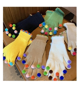 Guanti in maglia colorati con pompon decorativi esposti su una superficie di legno