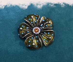Detailed close-up of a vintage flower brooch with blue rhinestones and green enamel petals