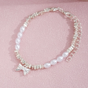 Detail of faux pearl bracelet with silver bow charm on a textured pink background