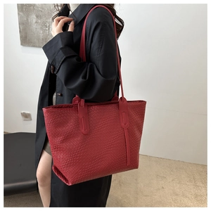 Sac cabas rouge à texture tressée porté avec un trench noir pour un look très élégant