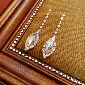 Detailed view of rose gold pear-cut crystal earrings on brown velvet with wood accents