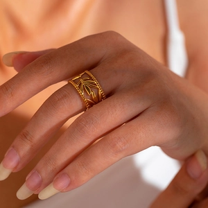Detail of bohemian gold-plated ring with woven leaf texture and beaded edges on finger
