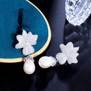 Macro detail of floral zircon studs with teardrop pearl drops on elegant silk background