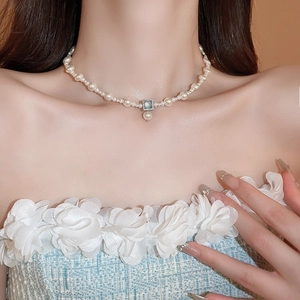 Detail of a gold-plated pearl necklace with a square blue gemstone pendant on a model