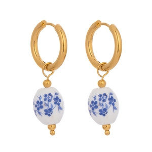 Detail of gold hoop earrings with white ceramic pendants featuring blue floral enamel patterns