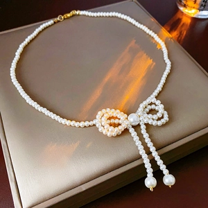 Detailed view of pearl bow necklace with dangling tassels on a gray jewelry box