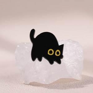 Lindo pin de esmalte de gato negro con ojos amarillos sobre fondo de piedra blanca