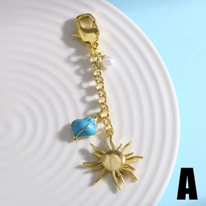Gold-plated sun pendant keychain with faux pearl and blue shell charm on ceramic