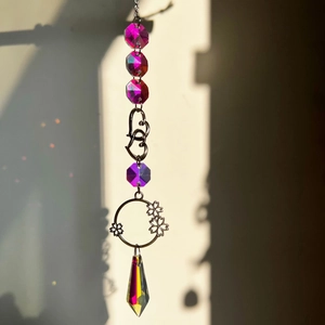 Detail of crystal hanging ornament featuring a pink bead and rainbow prism with suncatcher reflections