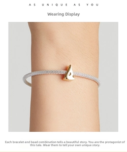 Close-up of a silver mesh bracelet featuring a unique golden cheese-shaped pendant on wrist