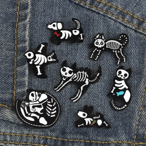Detailed view of cartoon skeleton animal enamel pins on a blue denim background