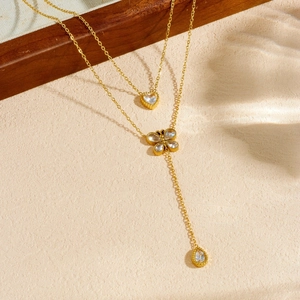 Gold layered necklace with butterfly and heart pendants on sand and wood surface