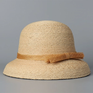 Detail showing the fine texture of beige raffia straw hat with golden mesh bow