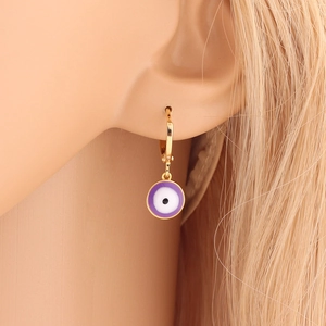Macro view of gold hoop earring with a purple enamel evil eye pendant on a model