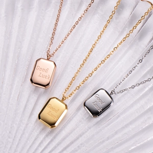 Detailed view of three metallic rectangle pendants engraved with Good Luck in rose gold