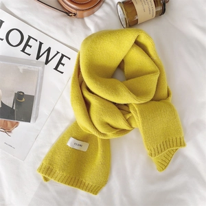 Close-up of yellow knitted scarf texture with white label on soft bedding