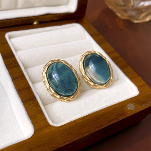 Macro shot of vintage gold-trimmed oval green gemstone earrings in a wood jewelry box