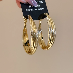 Détail de créoles plaquées or 18 carats avec couches de métal lisses et texturées croisées