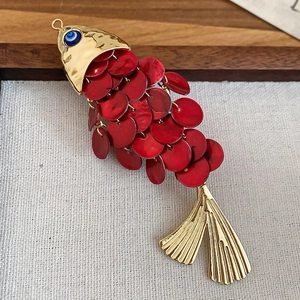 Macro detail of red shell fish hair clip with golden metal accents and blue evil eye bead