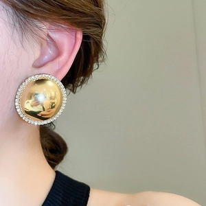 Close-up of a model wearing large gold dome earrings with a rhinestone border