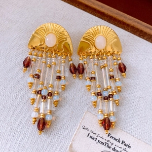 Détail de boucles d'oreilles dorées vintage avec pompons et pierres ovales blanches