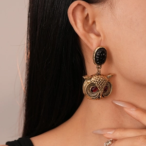 Detailed close-up of retro owl earrings with red gem eyes and black stone on model