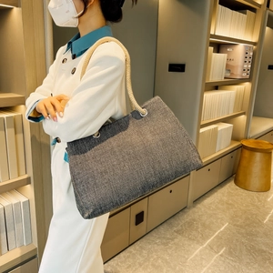 Detail of dark grey tote bag with thick rope handles carried by a model in a modern store