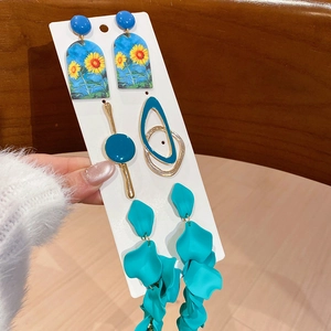 Detailed set of sunflower earrings and teal blue geometric pendants on a display card