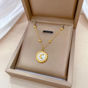Detail of gold moon shell pendant with hammered edge in a beige jewelry box