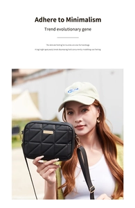 Detail of black quilted camera bag featuring a gold logo plate and wide fabric shoulder strap