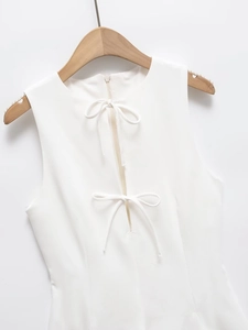 Detail of white sleeveless dress with bow accents and a hidden zipper on a wooden hanger