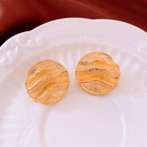 Detailed close-up of 18k gold-plated hammered disc earrings on a white vintage ceramic plate