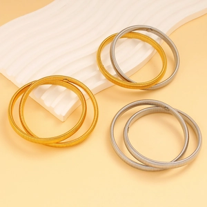 Close-up of golden and silver elastic metal spring bracelets on a wavy white stand