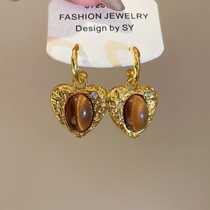 Close-up of heart-shaped gold earrings with brown tiger eye stones on display card