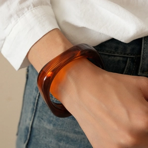 Close-up of a thick amber resin geometric bangle worn by a model in casual attire